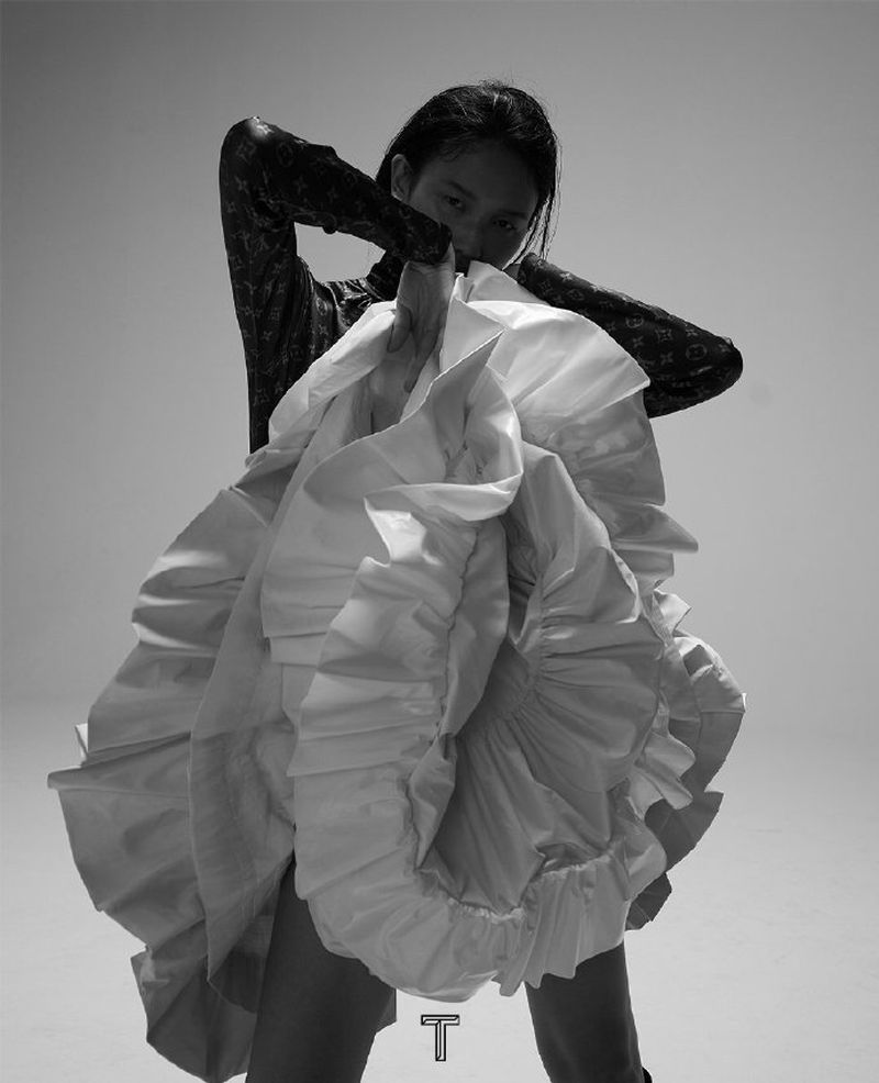 Model wearing a voluminous white ruffled skirt and patterned black top, posing in a dramatic editorial black-and-white fashion shoot."
